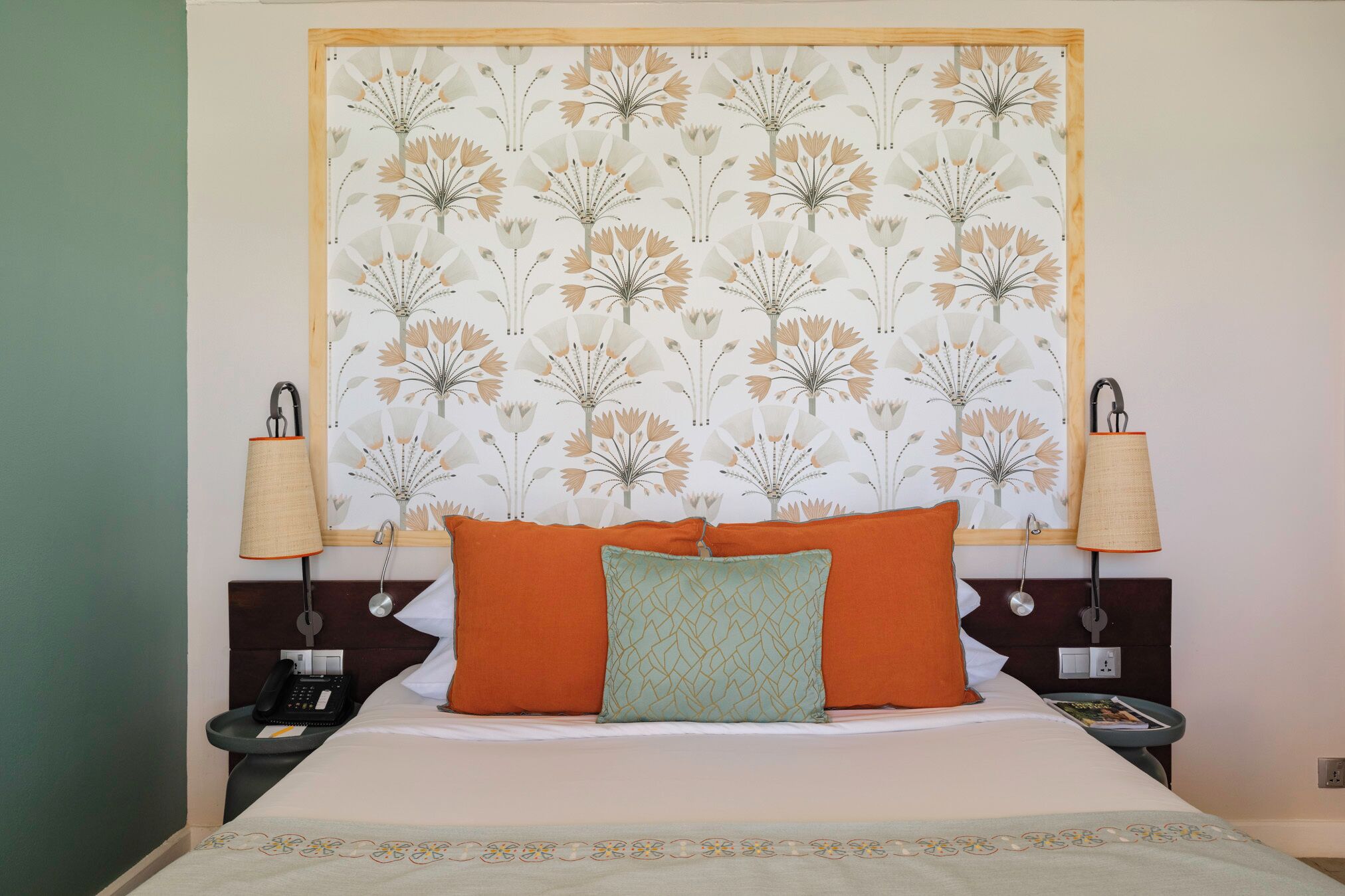A neatly made bed with two pillows, a bedside lamp, and a phone on a nightstand.