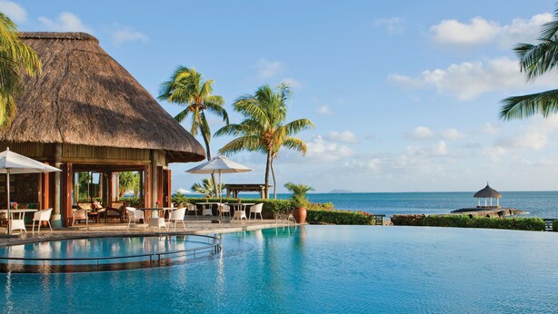 A pool area with a thatched-roof structure, palm trees, and a view of the ocean. - Veranda Paul & Virginie Hotel & Spa - Adults Only (Grand Gaube)