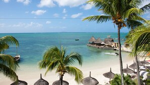 A beach resort with thatched-roof structures, palm trees, and a clear view of the ocean. - Veranda Paul & Virginie Hotel & Spa - Adults Only (Grand Gaube)