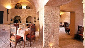 Zona pranzo con pareti in pietra, tavoli e sedie alti, soffitti a volta e ceramiche appese alle pareti.