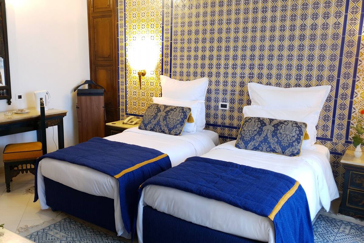 A hotel room with two beds, a desk, a chair, a telephone, and a mirror.