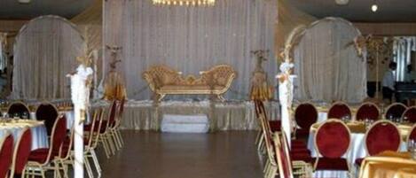 Un espacio para eventos formales con un escenario, sillas rojas y doradas, y una araña de cristal.