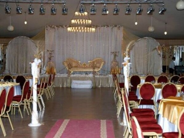 Un espacio para eventos formales con un escenario, sillas rojas y doradas, y una araña de cristal.
