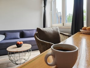 Ein gemütlicher Wohnbereich mit einer Couch, einem runden Couchtisch mit Früchten und einer Kaffeetasse auf einem Holztisch.