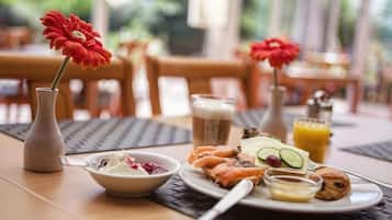 Un desayuno con un plato de comida, un vaso de jugo de naranja, una taza de café y un florero con una flor roja.