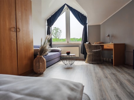Ein Schlafzimmer mit Bett, Sofa, Schreibtisch, Stuhl, einem Fenster mit Vorhängen und Blick ins Grüne.. Pure Hotel Dänischer Hof