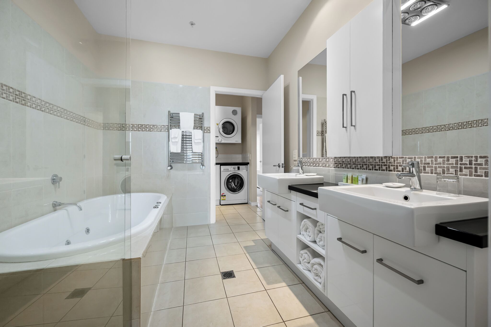 Un baño moderno con ducha de vidrio, una bañera independiente, lavadora integrada y un tocador con espejo.
