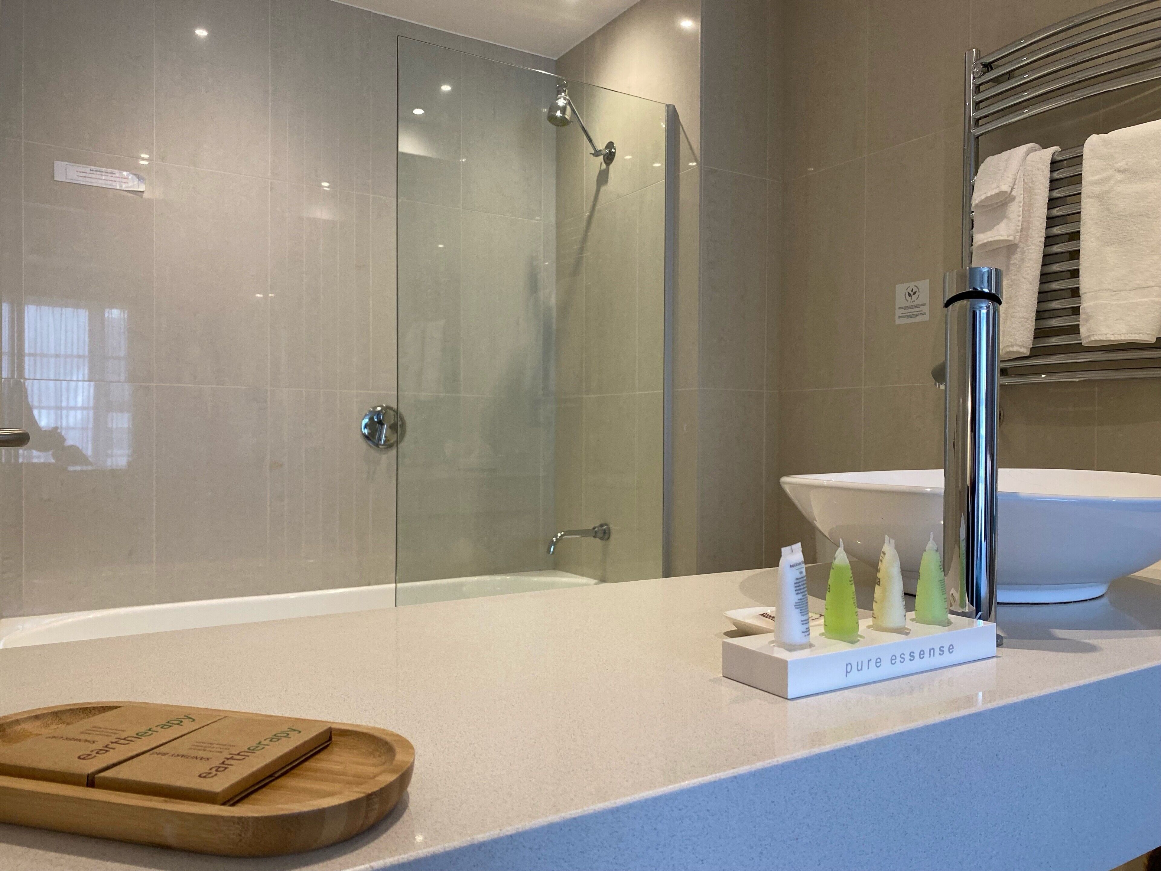 A modern bathroom with a glass-enclosed shower, a white sink, and a wooden tray with a bottle of Earththerapy soap.