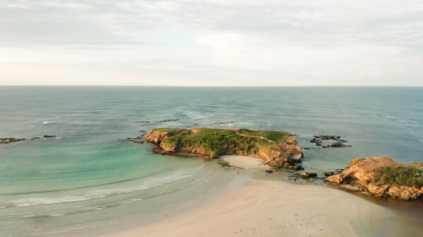 A coastal landscape with a sandy beach, rocky outcrops, and calm sea. - Deep Blue Hotel & Hot Springs (Warrnambool)