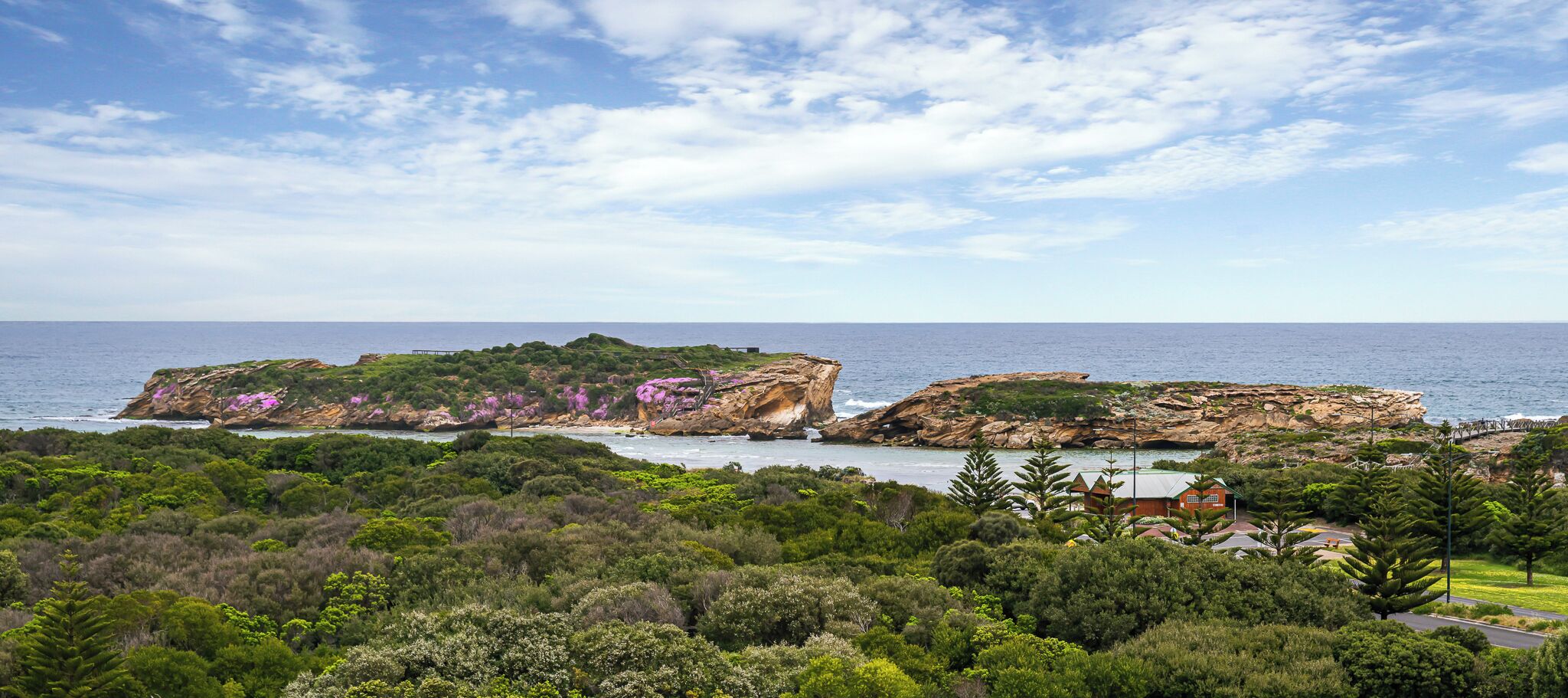 A coastal landscape with rocky outcrops and dense greenery.