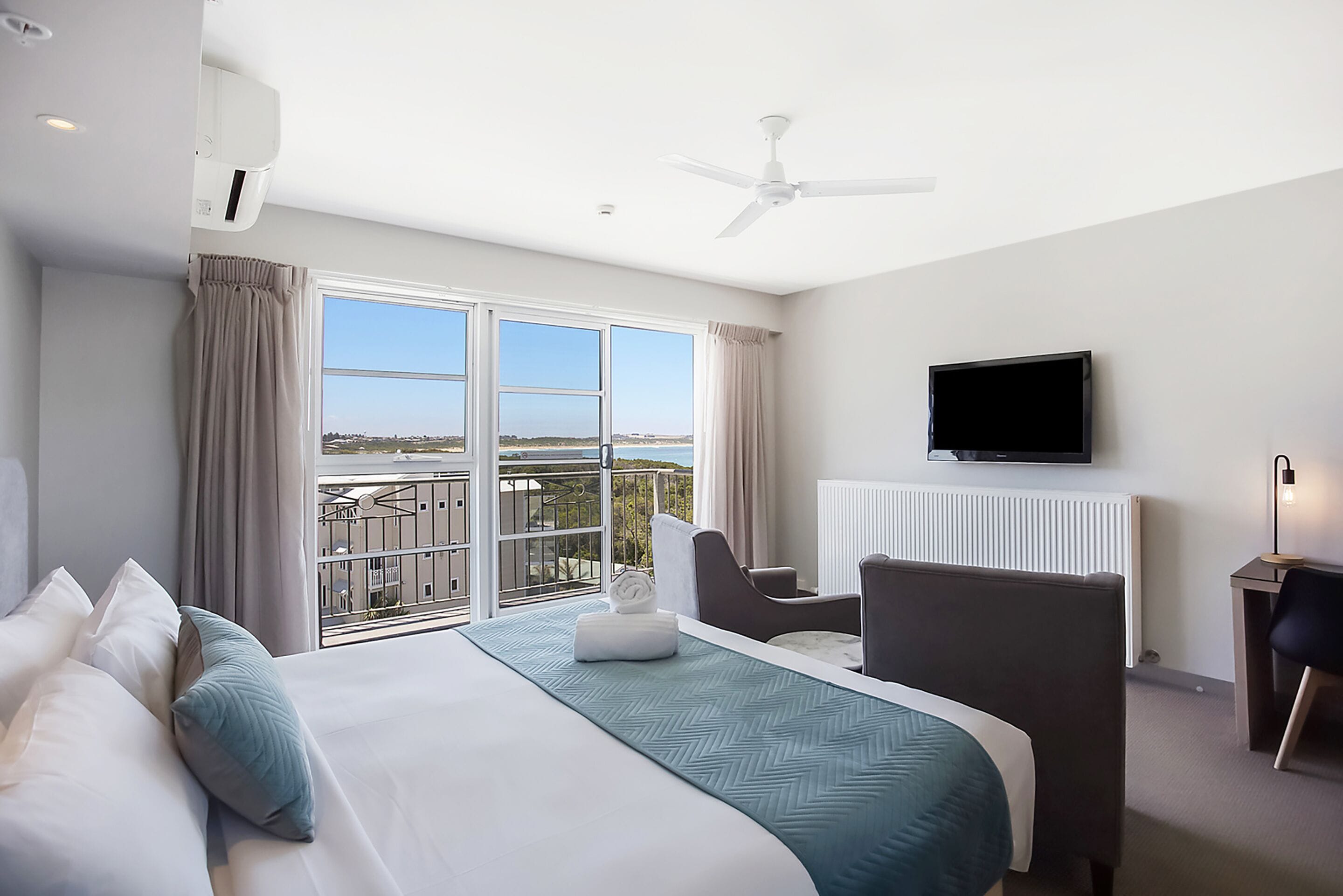 A hotel room with a bed, a desk, a chair, a television, and a balcony with a view.