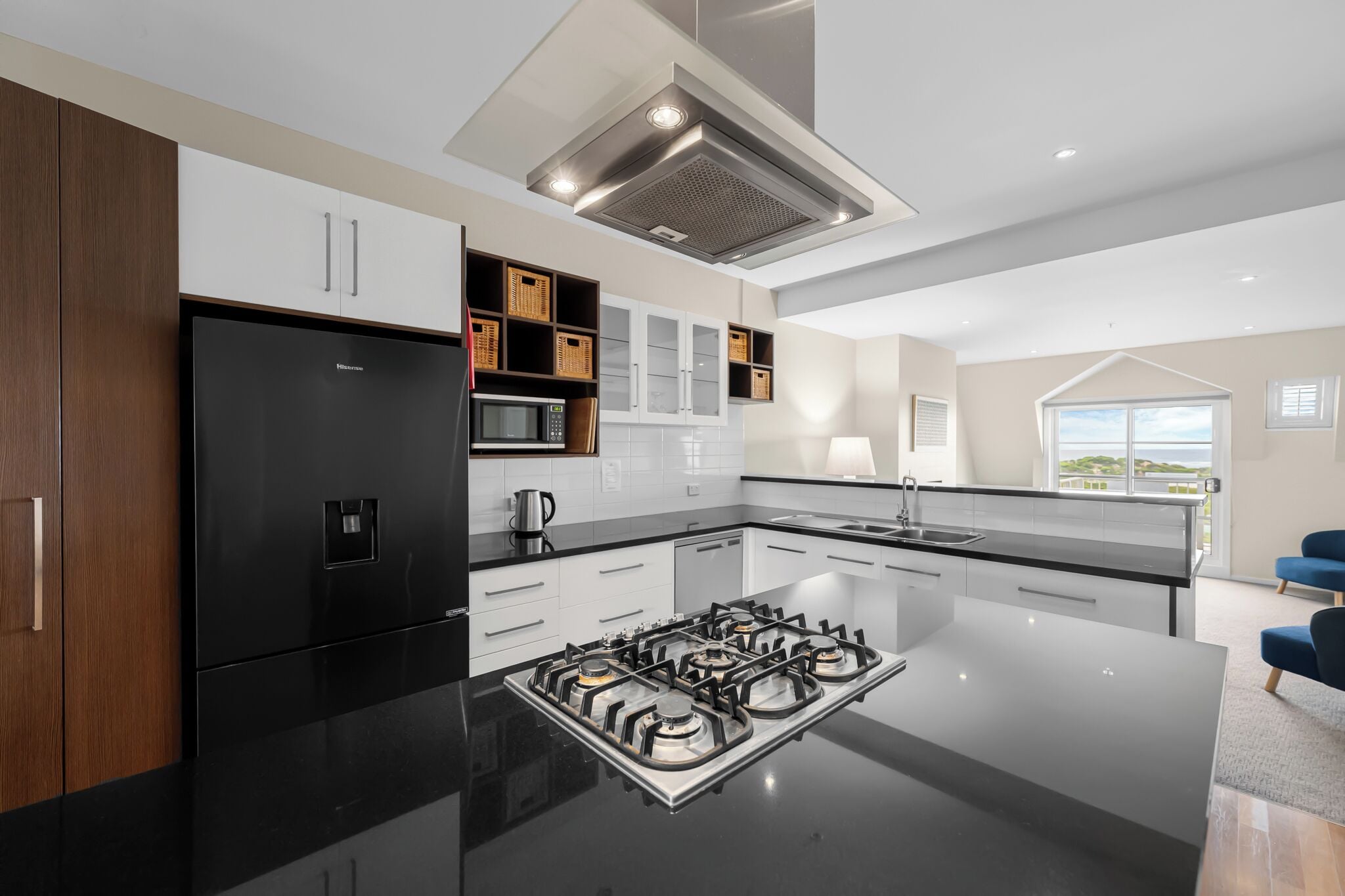 A modern kitchen with a black refrigerator, white cabinets, a gas stove, and a large window offering a view.