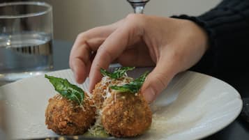 A hand placing a food item on a plate with a glass of red wine in the background.