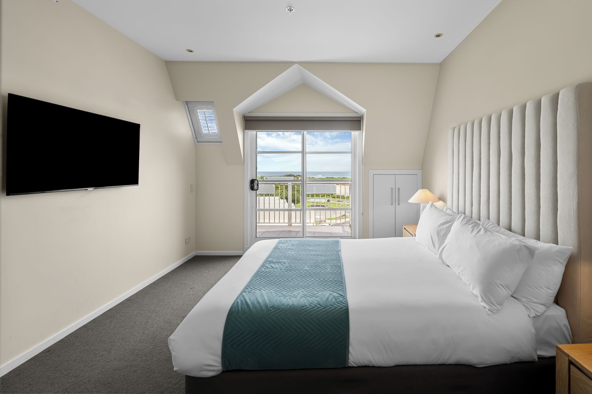 Une chambre d’hôtel dotée d’un grand lit, d’un téléviseur à écran plat fixé au mur, d’un balcon avec vue et d’une porte avec fenêtre.