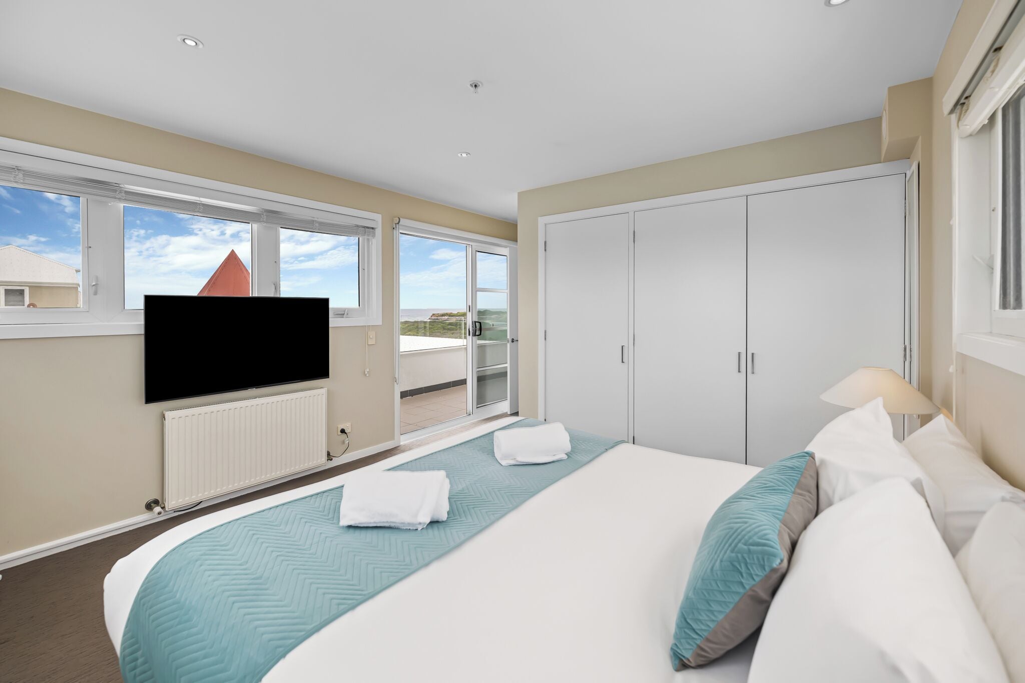 Habitación de hotel con una cama grande, un televisor de pantalla plana en la pared, un armario y un balcón con vistas a la ciudad.
