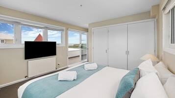 A hotel room with a large bed, a flat-screen TV mounted on the wall, a wardrobe, and a balcony with a view of the city.