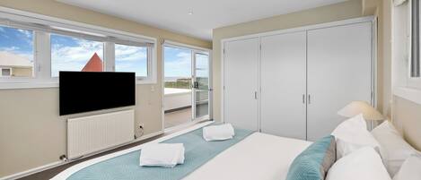 Habitación de hotel con una cama grande, un televisor de pantalla plana en la pared, un armario y un balcón con vistas a la ciudad.