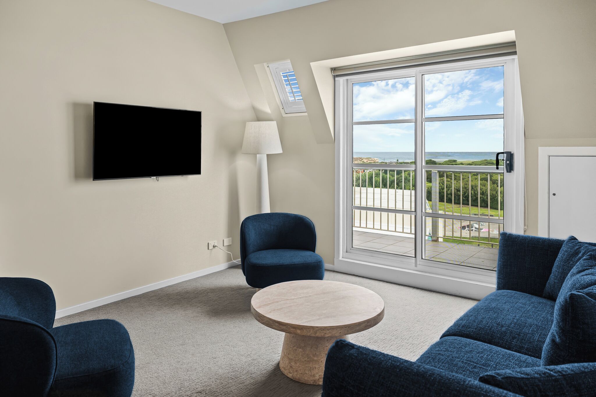 A modern living room with a flat-screen TV, a round coffee table, a blue armchair, and a sofa.
