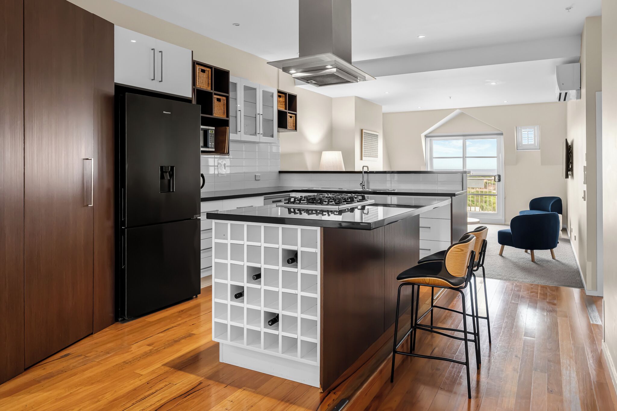 A modern kitchen with a central island, built-in wine storage, and a view to the outdoors.