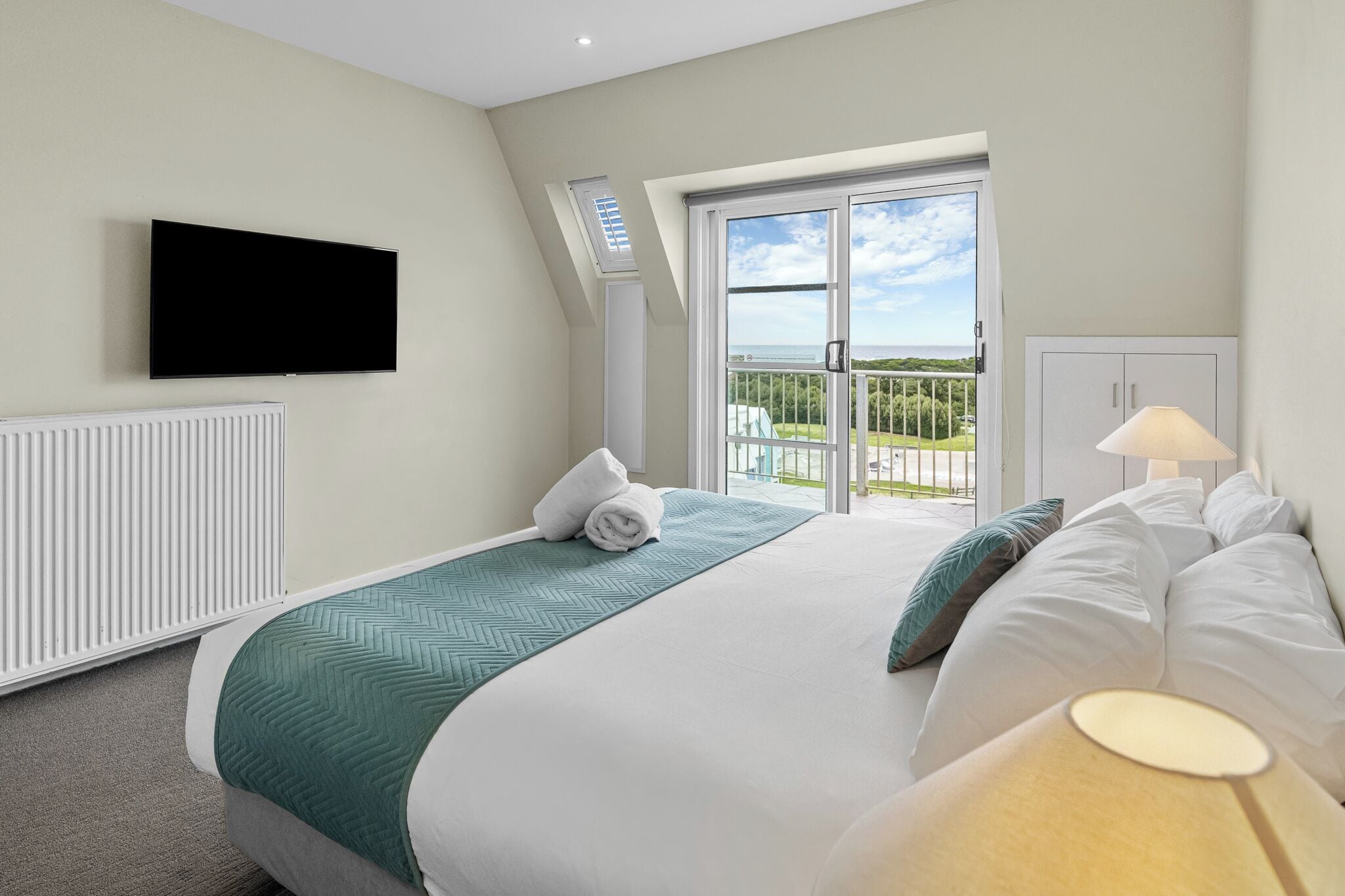 A hotel room with a bed, a TV, a window with a view, and a radiator.