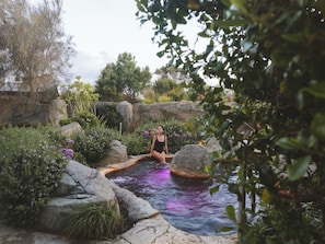 A person sitting by a water feature surrounded by rocks and greenery. - Deep Blue Hotel & Hot Springs (Warrnambool)