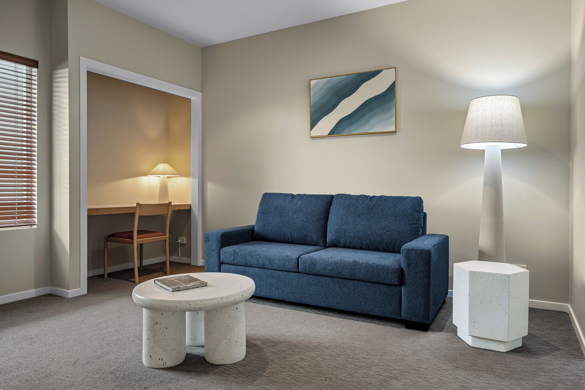 A living room with a blue sofa, a round coffee table, a floor lamp, a side table, and a painting on the wall.