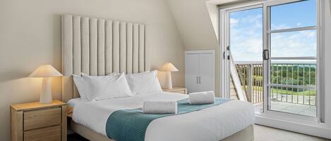 A bedroom with a bed, two bedside tables, a nightstand, a wardrobe, and a balcony with a view.