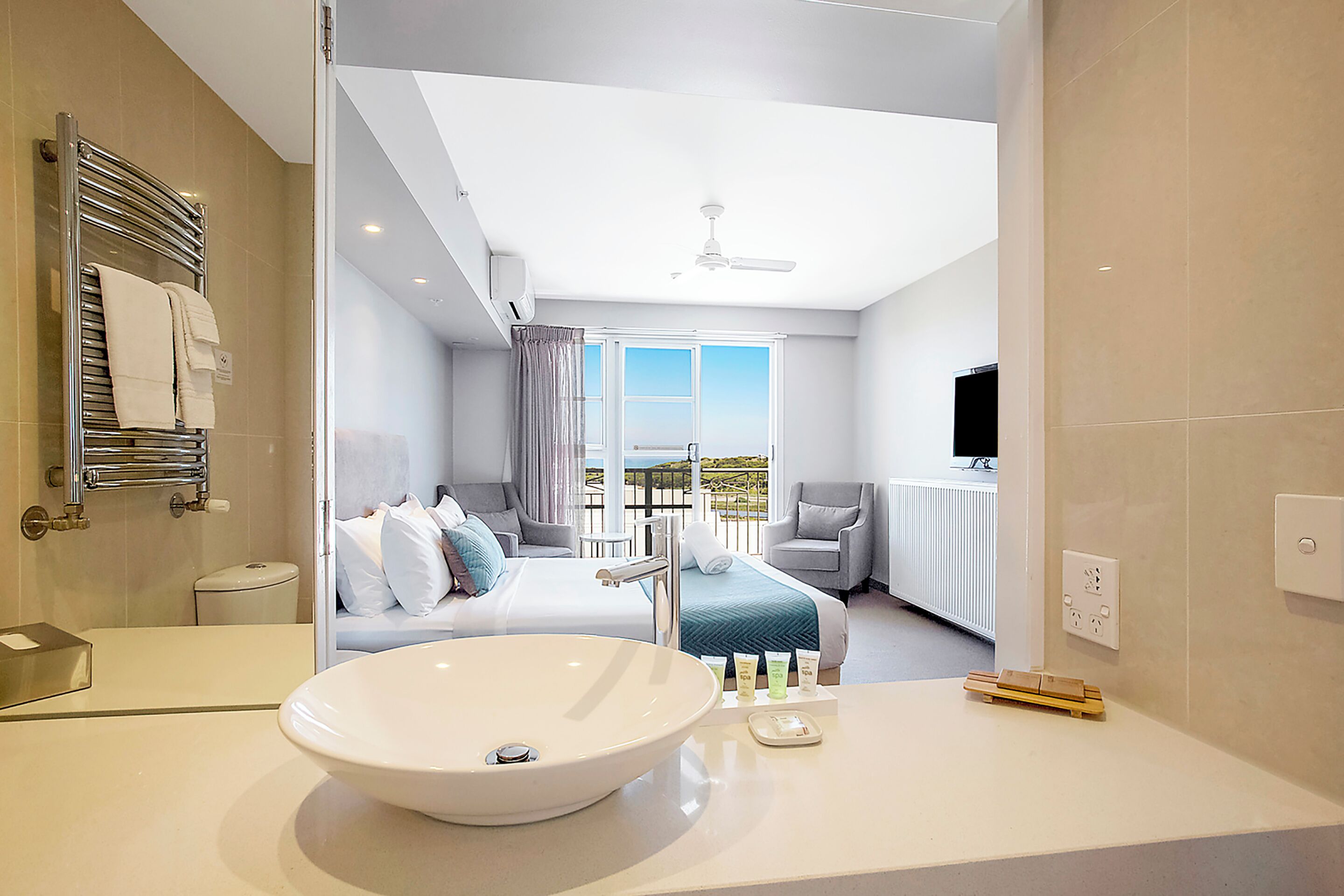 Un baño moderno con un lavamanos grande de color blanco, un espejo y un perchero para toallas.