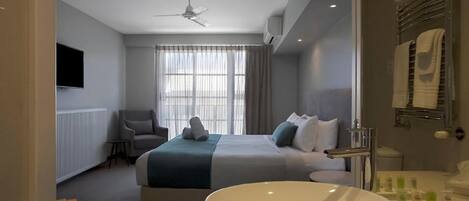 Habitación de hotel moderna con una cama grande, un lavamanos blanco redondo, un televisor y un ventilador de techo.