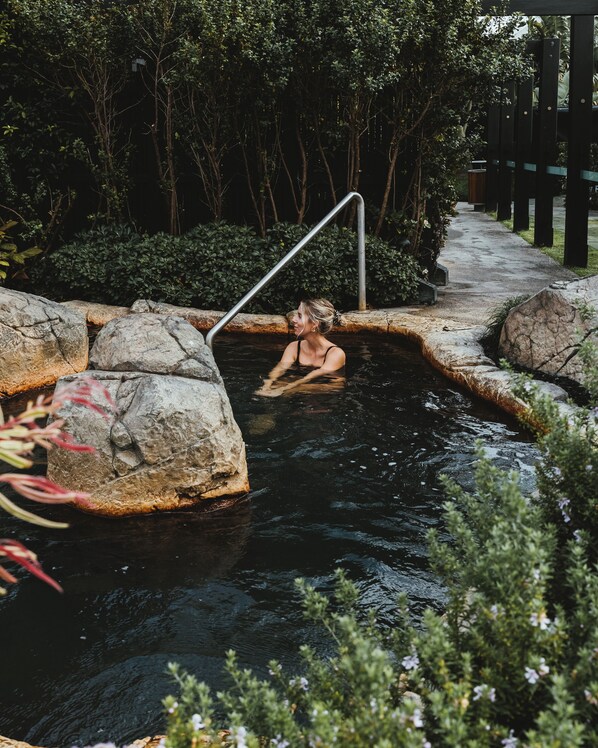 A person in a natural hot spring surrounded by rocks and greenery. - Deep Blue Hotel & Hot Springs (Warrnambool)