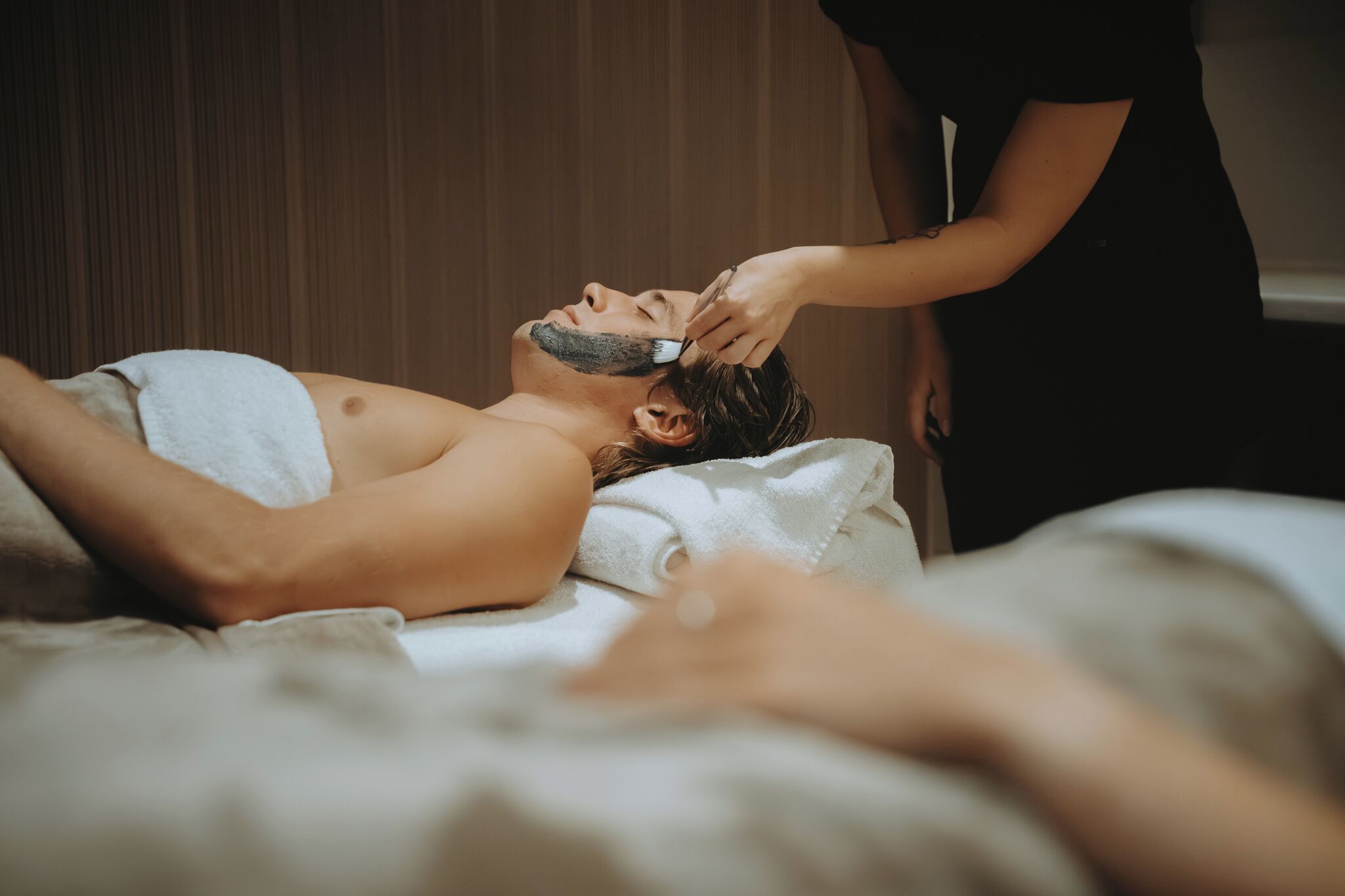 Eine Person liegt auf einem Bett und erhält eine Gesichtsbehandlung mit einem Handtuch.