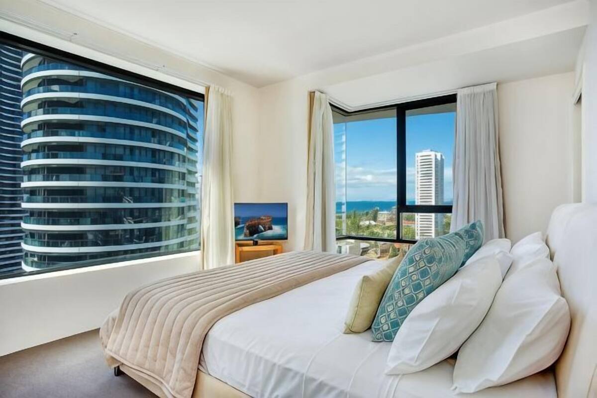 A hotel room with a large bed, a TV on a nightstand, a window with a view of a building, and a balcony.
