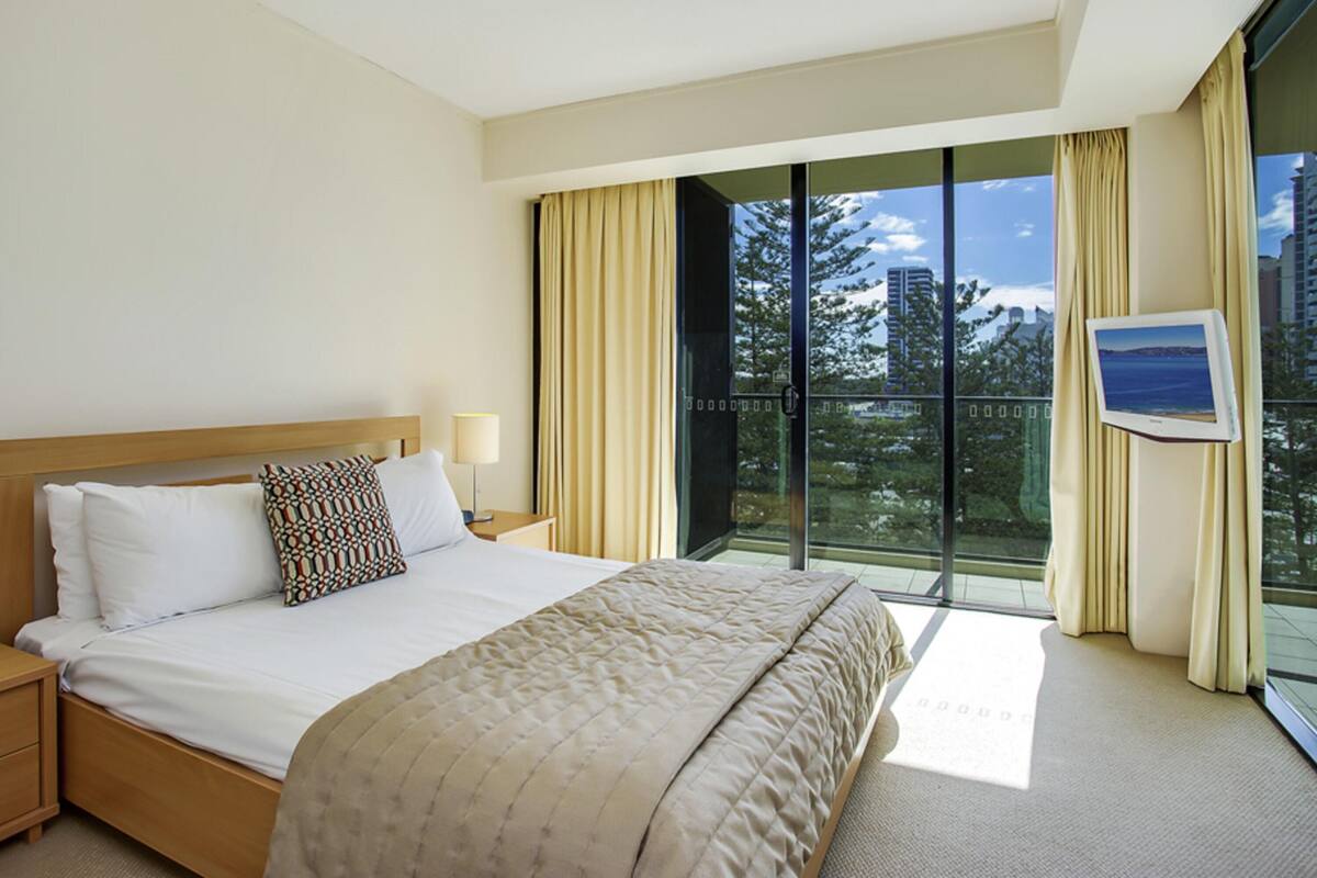 A hotel room with a bed, a nightstand, a window with curtains, and a view of the outdoors.