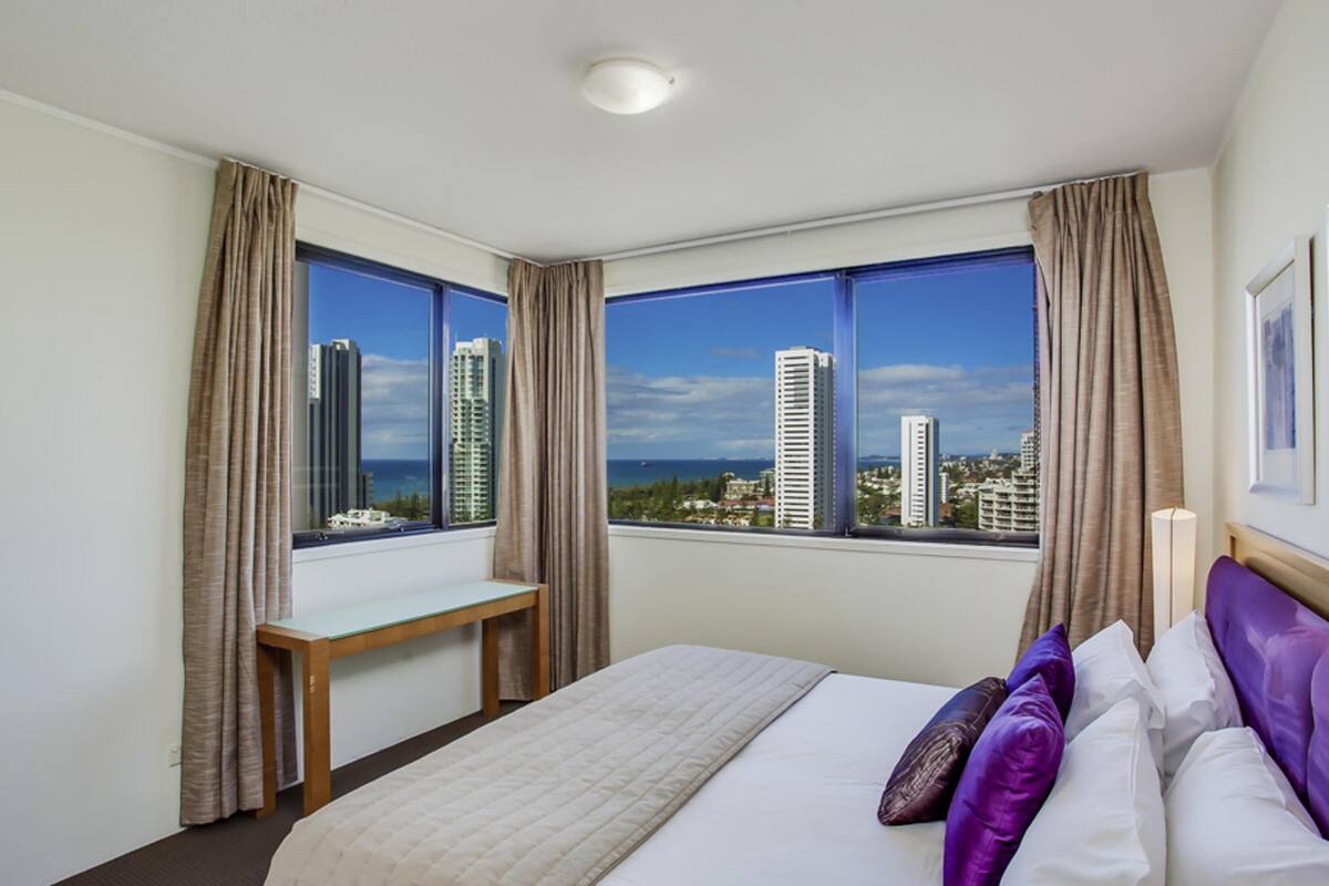 A hotel room with a bed, a desk, and large windows offering a city view.