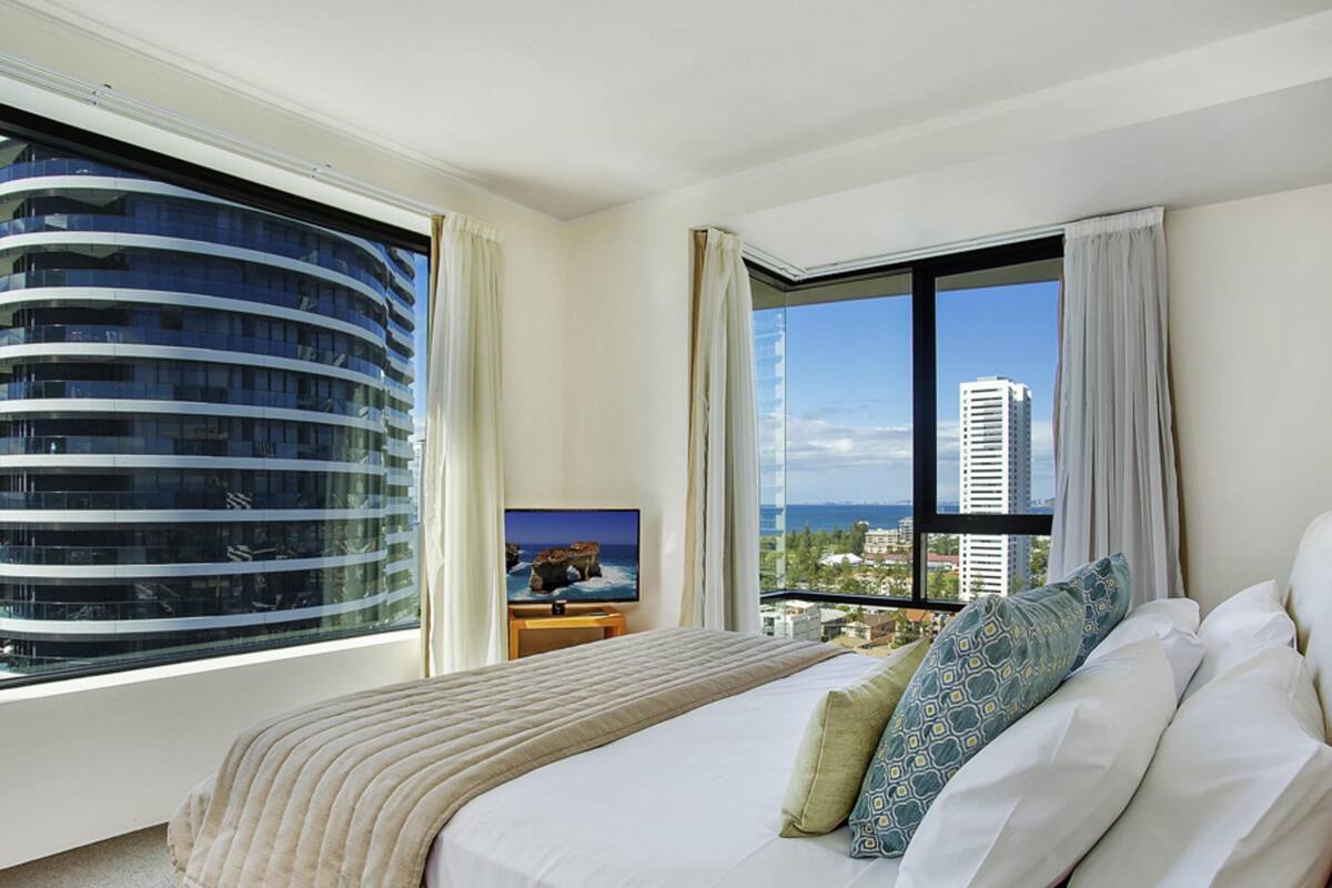 A hotel room with a large bed, a television, and a view of a cityscape through a large window.