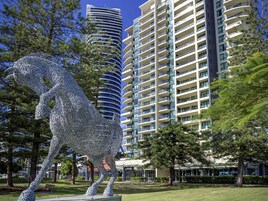 Una escultura de un caballo en un parque, con edificios modernos al fondo.
