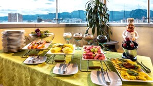 Una mesa de buffet con diversos platos y utensilios, una figurita de chef y una vista de un paisaje urbano con montañas al fondo.