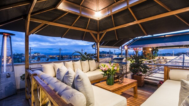 Una terraza en la azotea con un banco de madera, un sofá y una mesa adornada con flores.