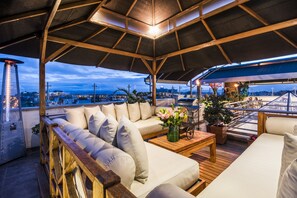 A rooftop deck with a wooden bench, a sofa, and a table with flowers.