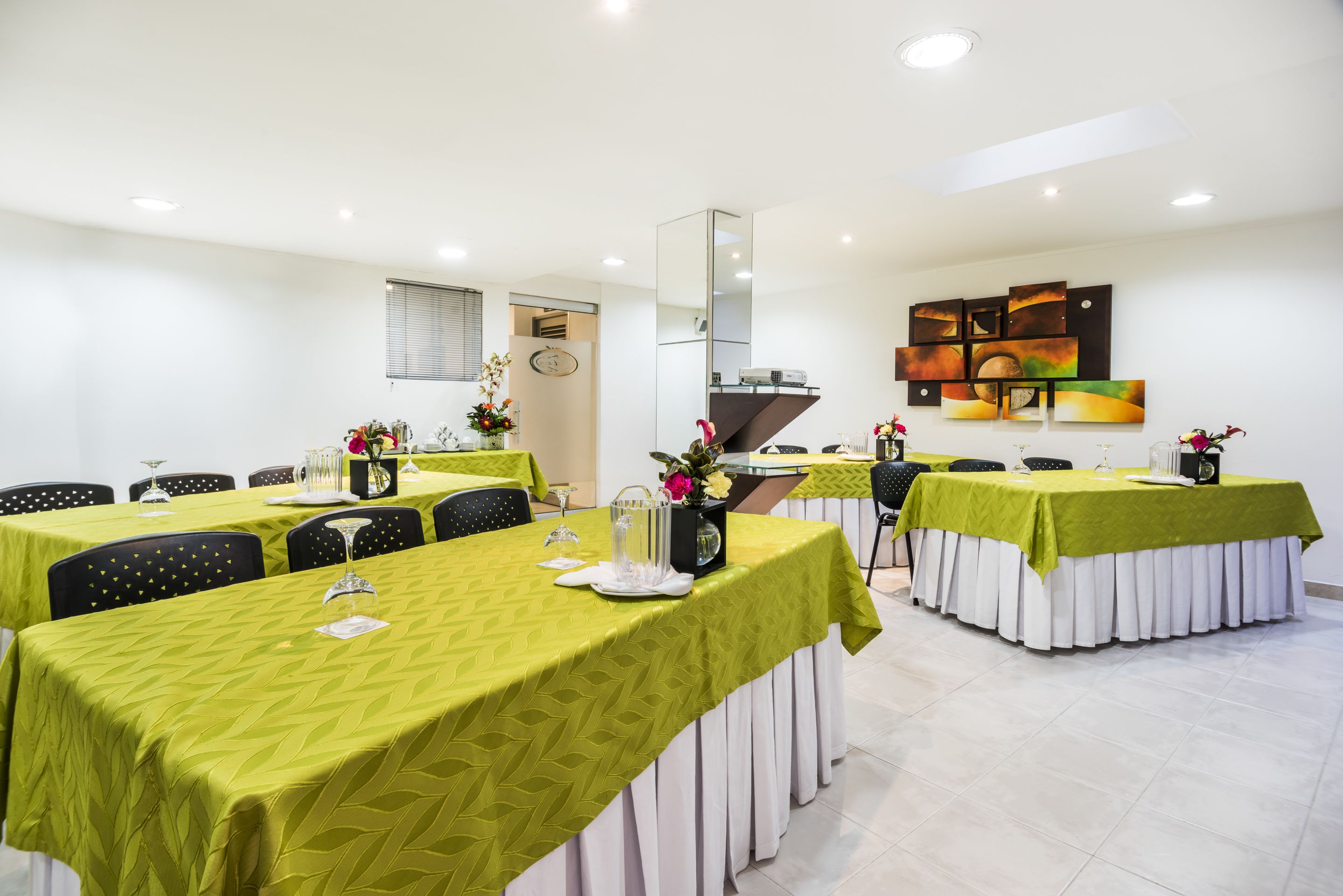 A dining area with tables covered in green tablecloths, chairs, and decorative centerpieces.
