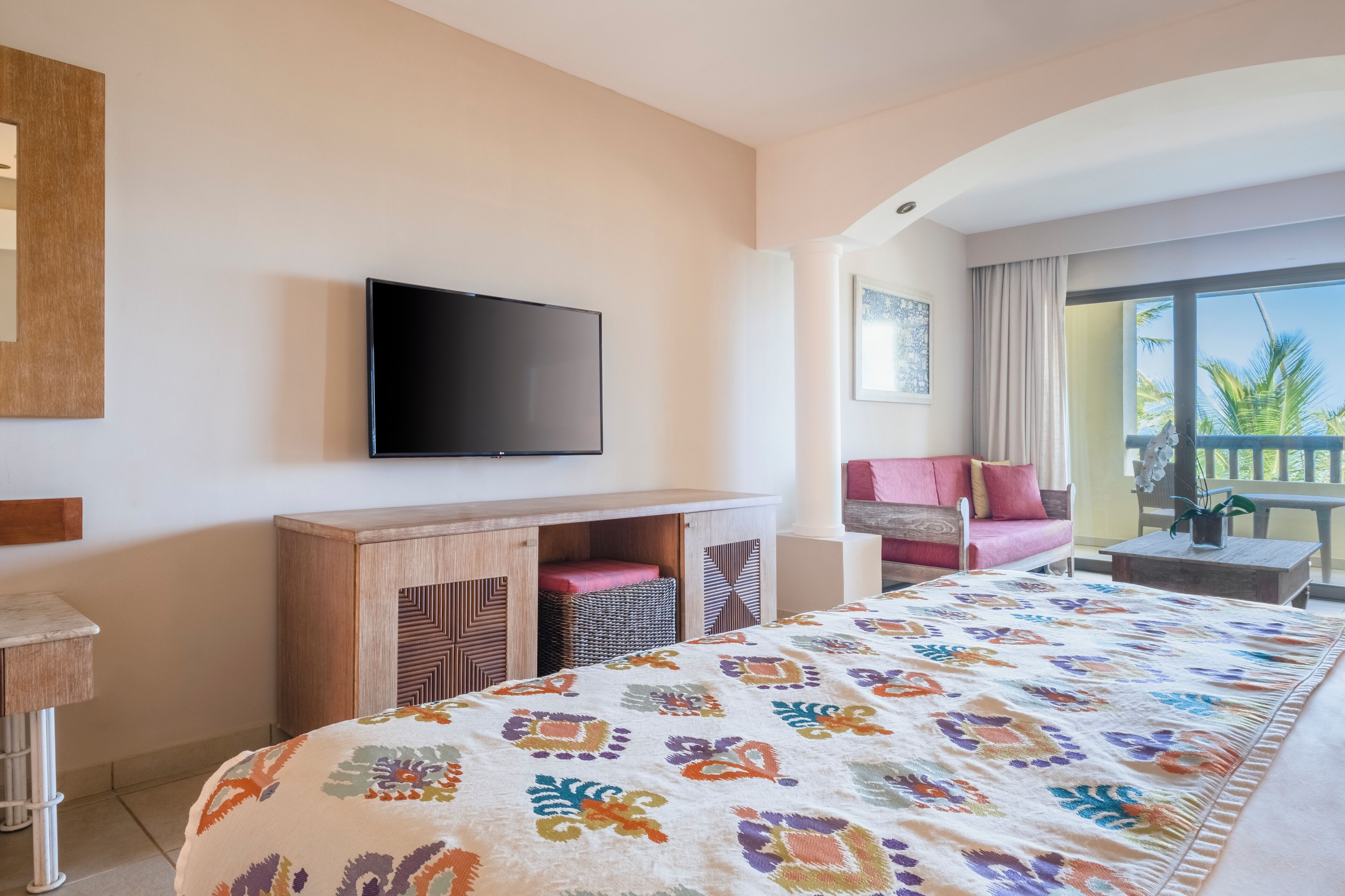 A hotel room with a bed, a television, a sofa, and a balcony with a view.