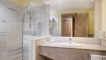 A modern bathroom with a glass-enclosed shower, a granite countertop sink, and a wooden door.