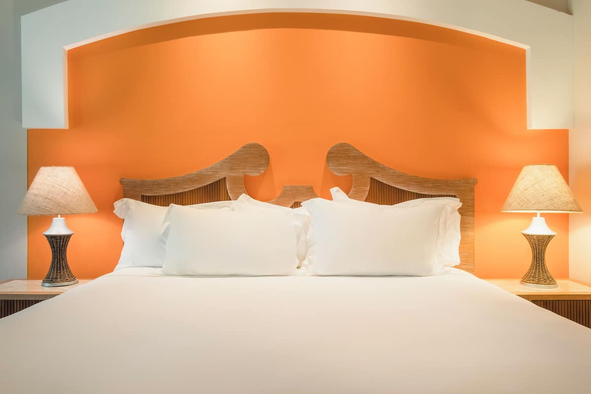 Un lit avec du linge de lit blanc, deux tables de chevet avec des lampes et un mur d’accent orange.
