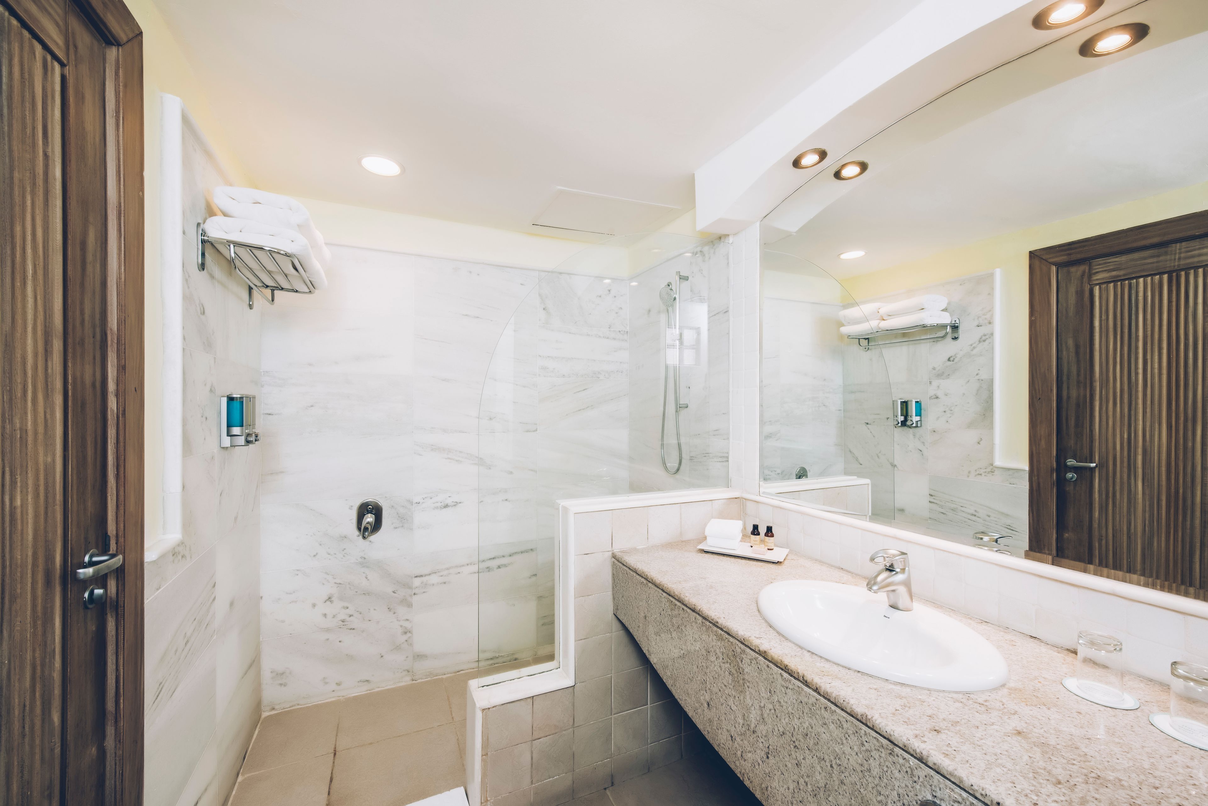 A modern bathroom with a marble shower, a large mirror, and a granite countertop.