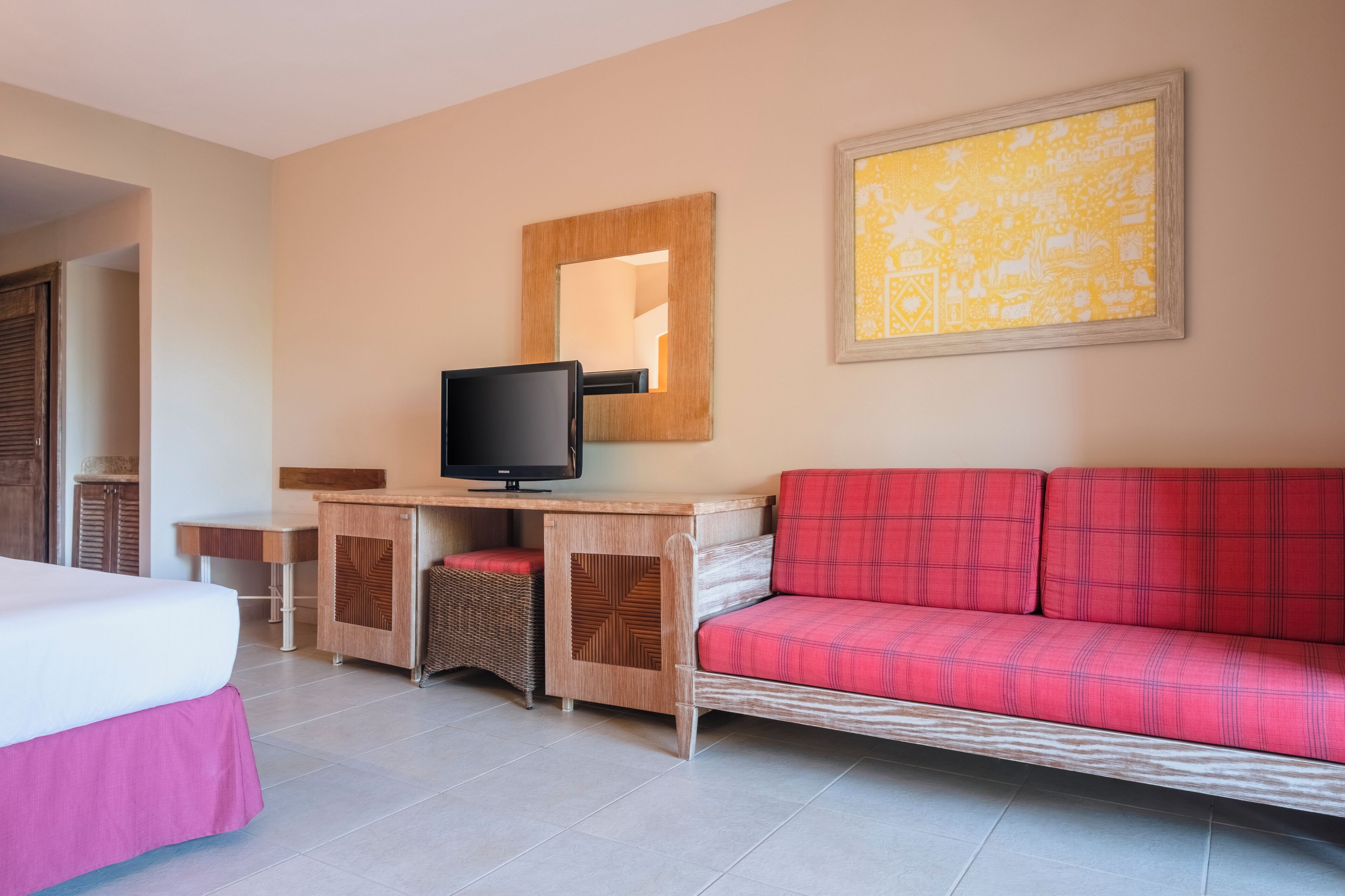 Ein Hotelzimmer mit einem Bett, einem Schreibtisch mit Fernseher, einem roten Sofa und einem großen, gerahmten Bild an der Wand.