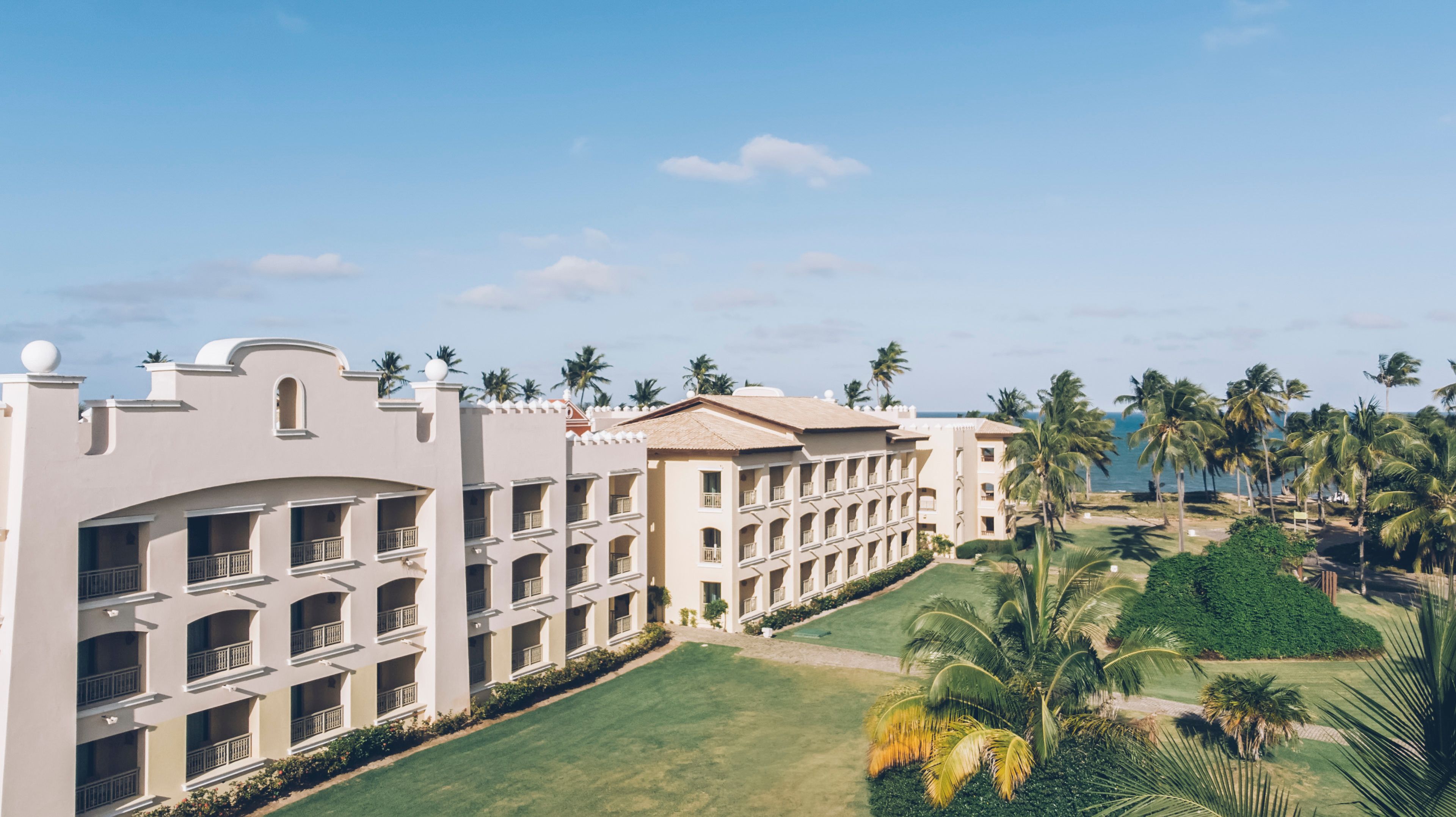 Un hotel con varios pisos, balcones y un césped bien cuidado con palmeras.