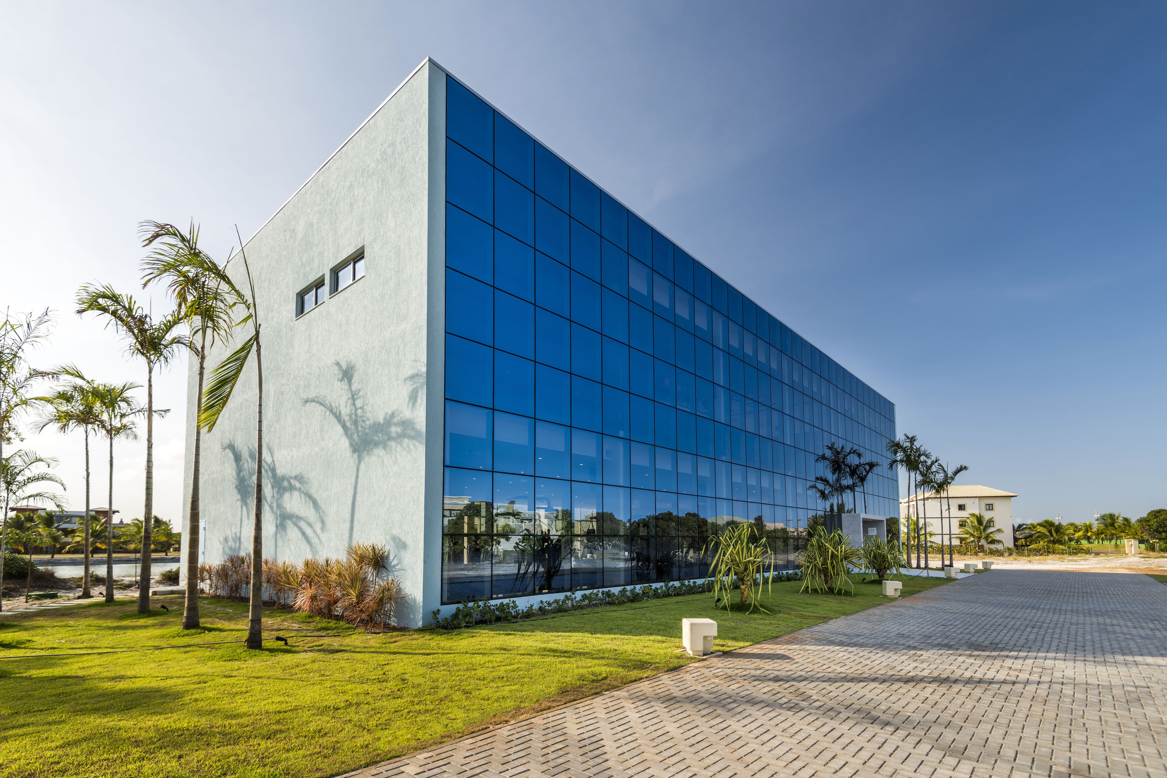A modern building with a glass facade, surrounded by a well-maintained lawn and palm trees.