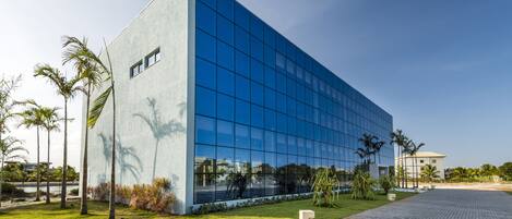 A modern building with a glass facade, surrounded by a well-maintained lawn and palm trees.
