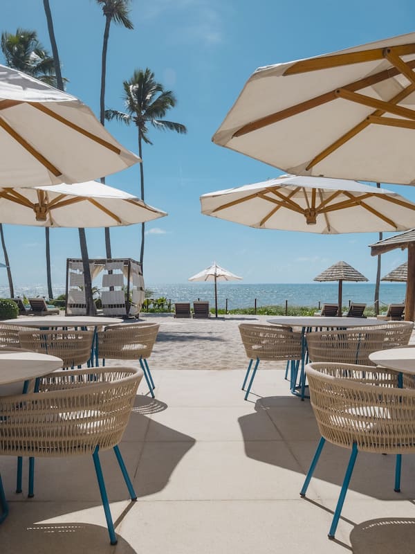 Relax by the ocean with a clear view of the beach from our outdoor seating area, featuring wicker chairs and umbrellas.