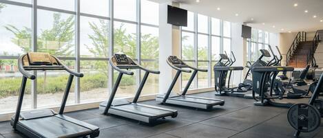 A gym with treadmills, weight machines, and a large window with a view of trees.